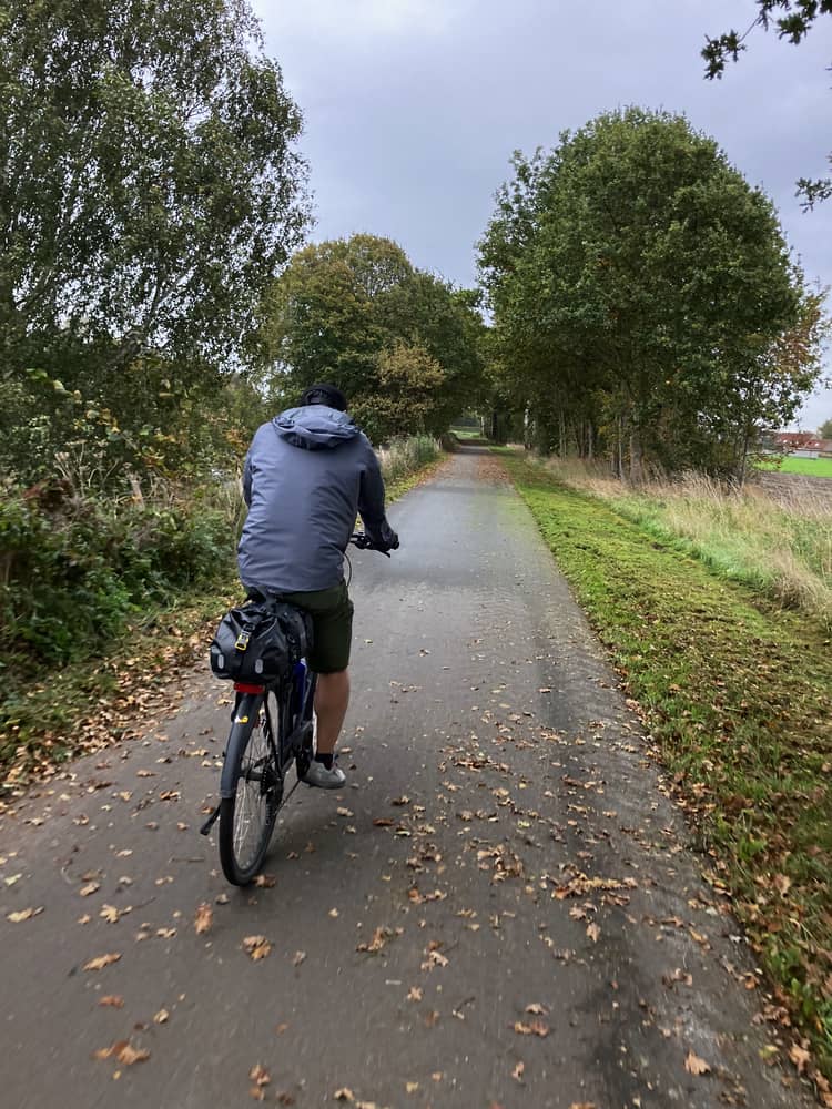 Un cycliste sur un chemin bordé d'arbres et de feuilles d'automne, pédalant dans un environnement naturel paisible.